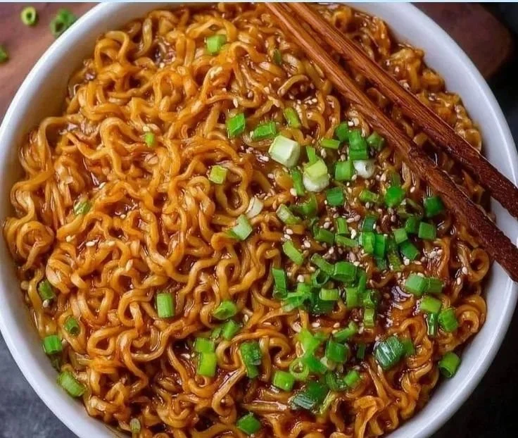 Bowl of easy saucy ramen noodles garnished with green onions and sesame seeds.