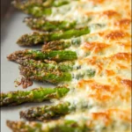 Plate of cheesy baked asparagus topped with melted cheese and herbs
