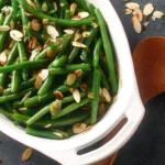 Plate of green beans almondine garnished with almonds and lemon