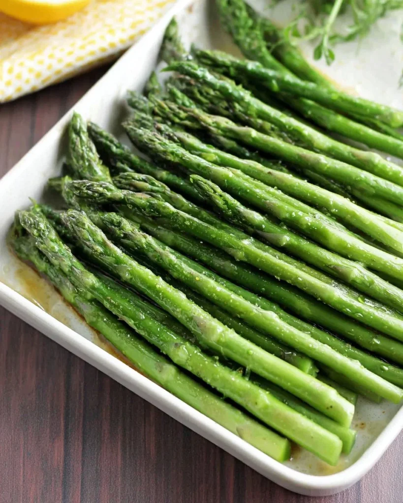 Simple 15-minute steamed asparagus served on a plate with lemon wedges.