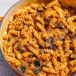 Creamy eggplant pasta dish garnished with fresh herbs and cheese