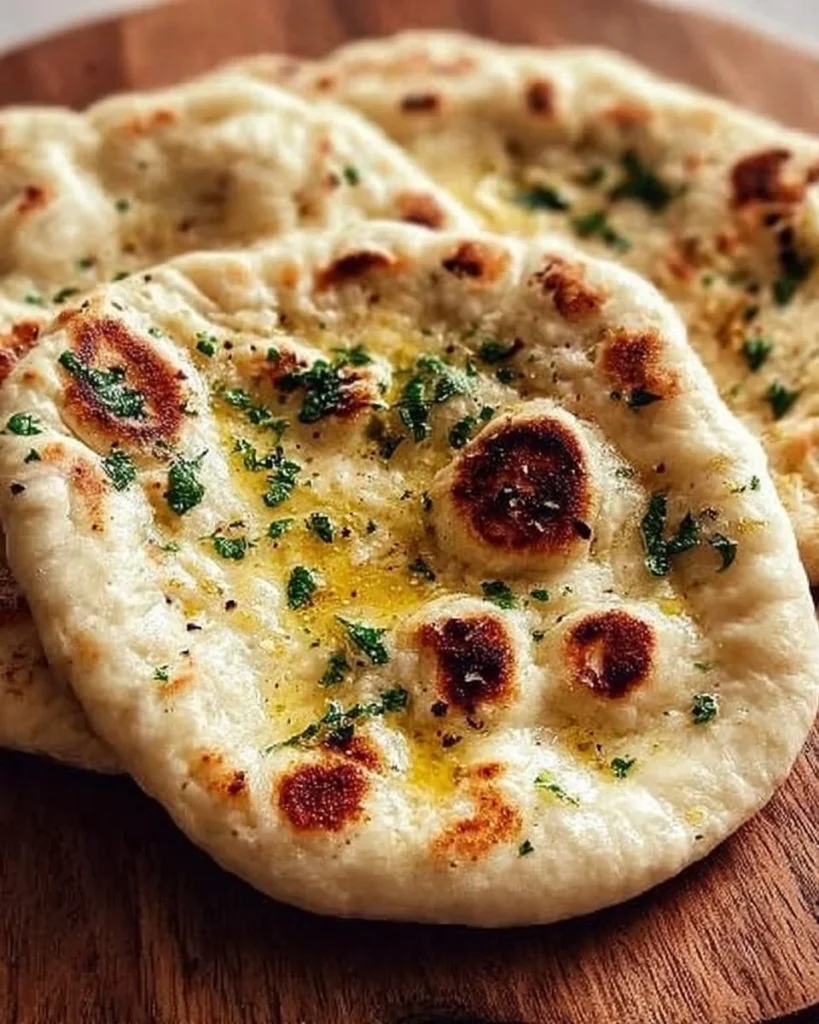 Freshly made homemade naan with garlic and herbs on a wooden table.