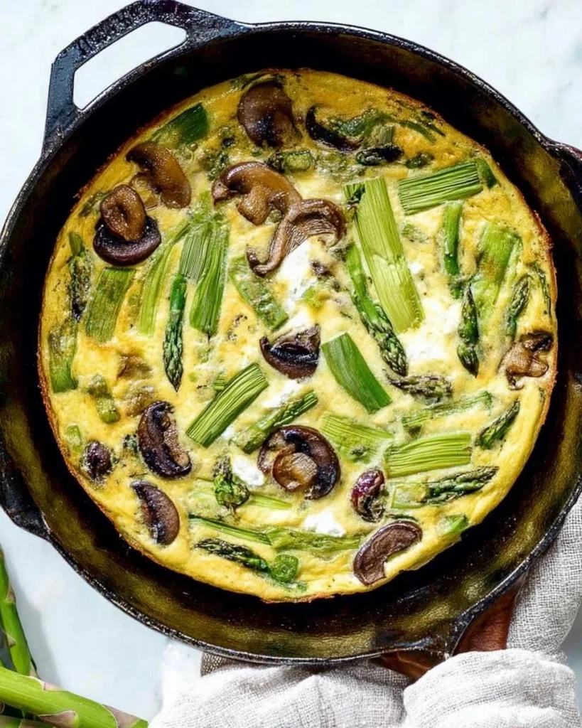 Mushroom and asparagus frittata topped with creamy goat cheese in a skillet
