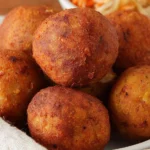 Golden deep fried plantain balls served on a plate with dipping sauce