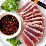Seared tuna steak garnished with herbs and served with dipping sauce