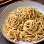 Plate of delicious sesame noodles garnished with green onions and sesame seeds.