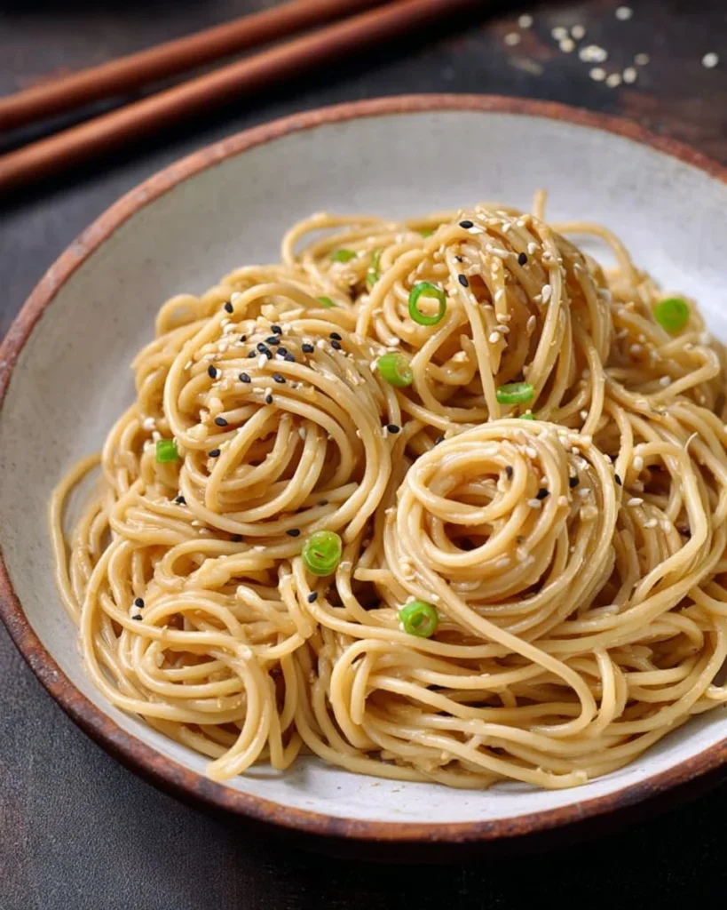 Plate of delicious sesame noodles garnished with green onions and sesame seeds.