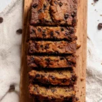 Loaf of oat flour banana bread with slices on a wooden cutting board.