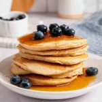 Stack of fluffy oat flour pancakes topped with fresh berries and syrup