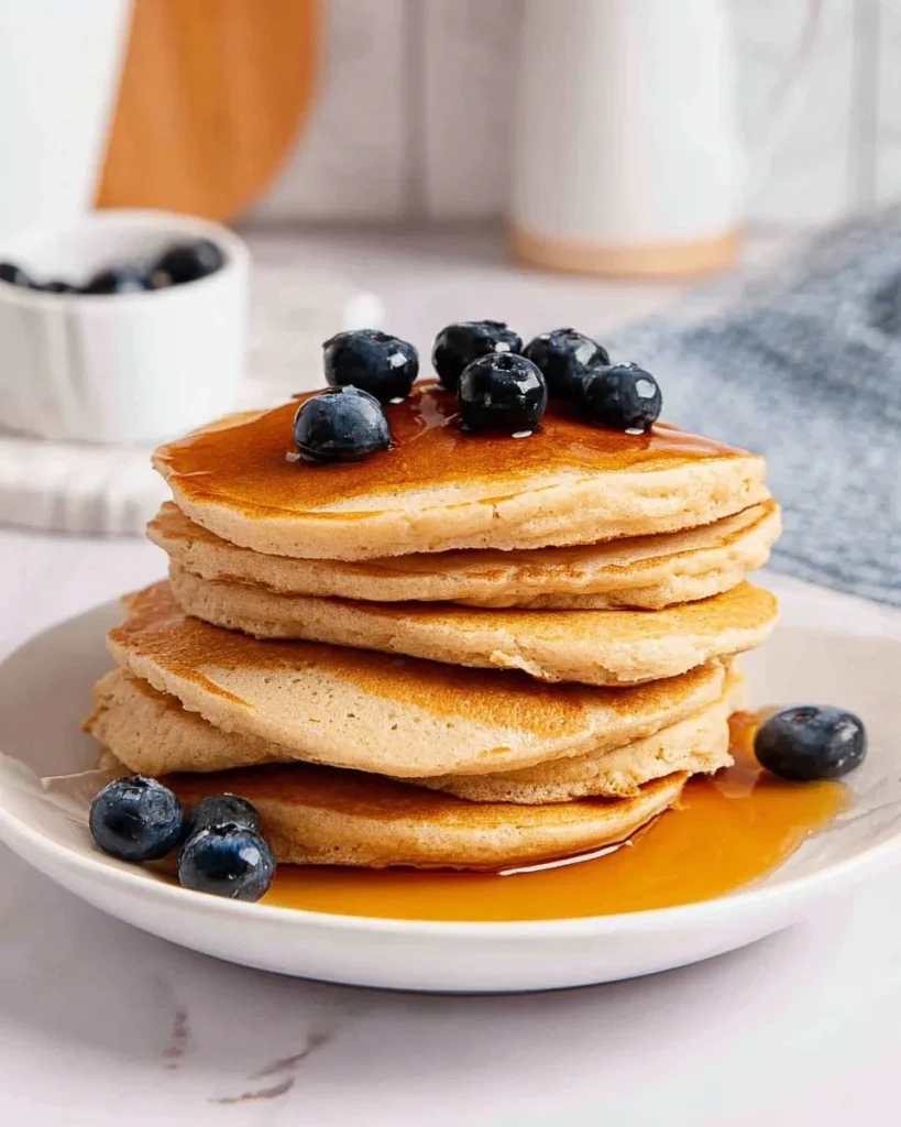 Stack of fluffy oat flour pancakes topped with fresh berries and syrup