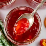 Homemade red pepper jelly in a jar with fresh peppers and herbs