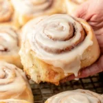 Freshly baked Amish cinnamon rolls with frosting on a wooden table