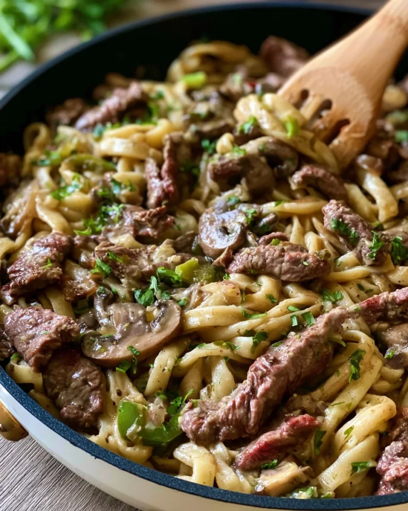A delicious plate of cheesesteak pasta topped with melted cheese and fresh herbs.