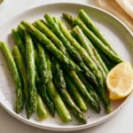 A plate of beautifully steamed asparagus garnished with lemon and herbs.